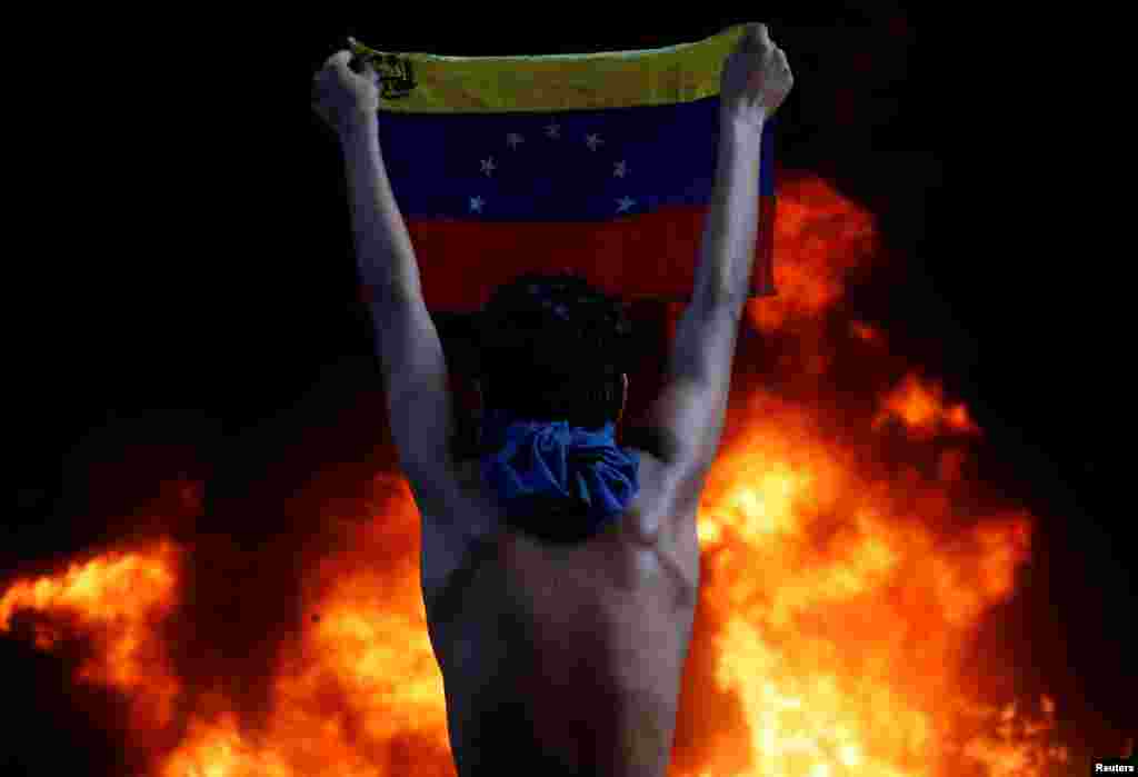 A protester holds a national flag as a bank burns during a rally against Venezuela&#39;s President Nicolas Maduro, in Caracas, Venezuela, June 12, 2017. (Reuters/Carlos Garcia Rawlins)