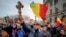Демонстрант против вакцинација држи дрвен крст додека другите веат национални знамиња за време на протестите во Букурешт во март 2021 година.