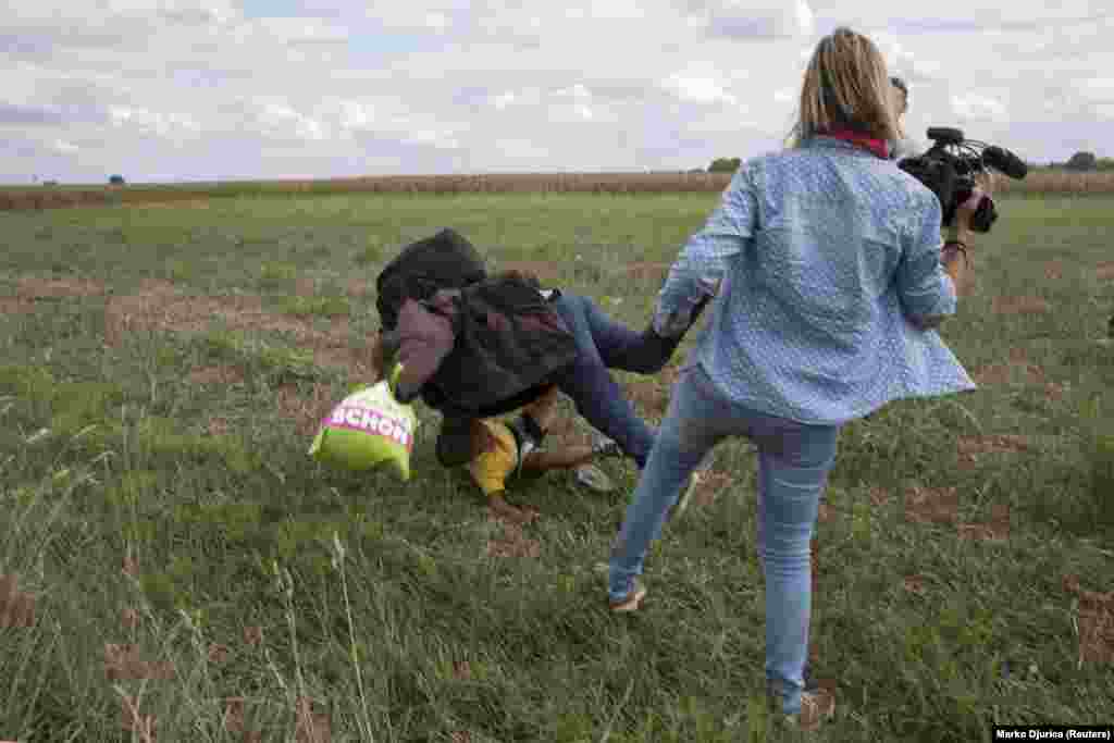A migrant carrying a child falls after tripping over TV camerawoman Petra Laszlo (right) while trying to escape from a collection point in Roszke village, Hungary, September 8, 2015. (Reuters/Marko Djurica)