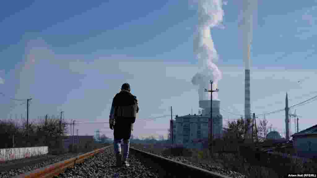 Një burrë duke ecur nëpër një hekurudhë ndërsa në sfond shihen tymtarët e termocentralit në Obiliq që lirojnë gazra të cilat e ndotin ajrin. Sipas Organizatës Botërore të Shëndetësisë (OBSH), ndotja e ajrit nga industria dhe ndotja e ajrit në shtëpi janë shqetësime të mëdha shëndetësore në Kosovë.