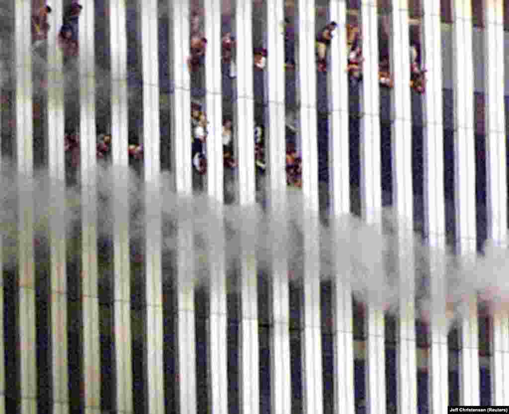 Из окон горящей Северной башни Всемирного торгового центра выглядывают люди, которые оказались в ловушке. Некоторые машут рукой, моля о помощи