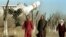 Kazakhstan -- Three local women pass by a copy of Soyuz space craft