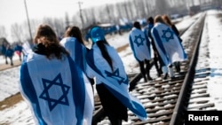 Люди c израильскими флагами на плечах идут по железнодорожным путям бывшего нацистского лагеря смерти Биркенау (Аушвиц II) в Освенциме-Бжезинку на юге Польши, 8.04.2013