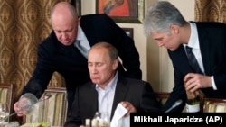 Evgheni Prigojin (stânga), patronul grupării de mercenari Wagner și poreclit «bucătarul lui Putin», servindu-l pe acesta la masă în restaurantul său de lux, 11 noiembrie, 2011. 