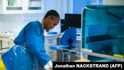 A Karolinska Kórház laboratóriumának orvosi személyzete a PCR-vizsgálat során használt géppel 2020. december 7-én, a Stockholm melletti Solnában