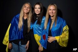 Ksenia Schnaider (balról), Elena Reva és Nágya Dzsjak ukrán zászlóval pózol a fotósoknak a színfalak mögött a 2023. szeptember 19-i, keddi londoni fellépésen