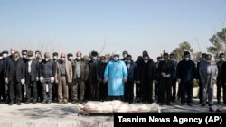 Mourners wearing face masks and gloves pray over the body of a former official in the Islamic Revolutionary Guards Corps, Farzad Tazari, who died on May 9 after being infected with the new coronavirus, at the Behesht-e-Zahra cemetery just outside Tehran on March 10.