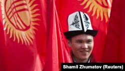 Кыргызстандын туусунун алдында ак калпак кийип турган жигит. 