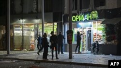 Орус армиясынын чабуулунан талкаланган соода борборунун алдында турган жергиликтүү тургундар. 29-март, 2025-жыл. Харьков.