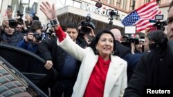 Президент появилась во дворе дворца Орбелиани, облаченная в тот же наряд, что и на своей инаугурации шесть лет назад: белое пальто и красная блузка, цвета национального флага Грузии