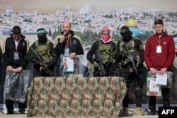 Tri pengjet izraelite qëndrojnë në podium pranë militantëve të Hamasit, pasi u liruan të shtunën, 15 shkurt.