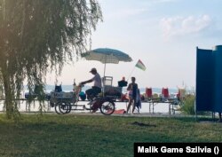 Vakáció a magyar tengeren: kukoricát és kürtőskalácsot árul egy kerékpáros árus a siófoki Aranyparton 2021. július 23-án