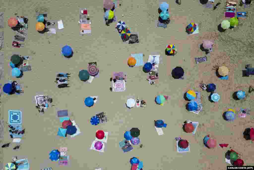Луѓето се сончаат на плажата Коста да Капарика, во Алмада, во близина на Лисабон, Португалија, на 29-ти јуни.