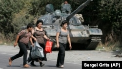 Refugiați georgieni trec prin fața unui tanc rusesc în satul Igoeti, la 50 km de Tbilisi, august 2008