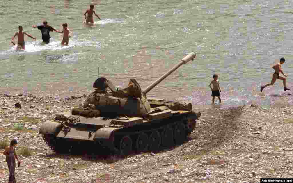 Беженцы из Косова купаются в реке. На берегу - танк албанской армии. Окрестности города Кукес, Албания, 6 июня 1999 года. &nbsp;