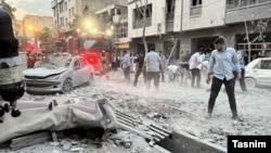 Израильдің шабуылынан бүлінген нысандар маңында жүрген адамдар. Тегеран, 13 маусым, 2025 жыл.