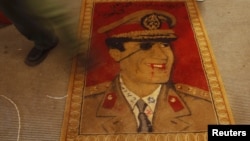 چهره معمر قذافی رهبر لیبی روی فرشی زیر پای معترضان در شهر بنغازی در سال ۲۰۱۱ 