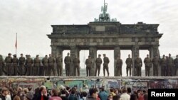 ГДРдин чек арачылары Бранденбург дарбазасынын алдындагы Берлин дубалынын үстүндө тизилип турушат. 11-ноябрь 1989