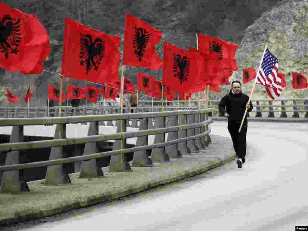 Етнички Албанец носи американско знаме на патот по кој се наредени албански знамиња во гратчето Качаник, на Косово, на 16 февруари, еден ден пред прославата на третата годишнина од прогласувањето на независноста на Косово од Србија. 