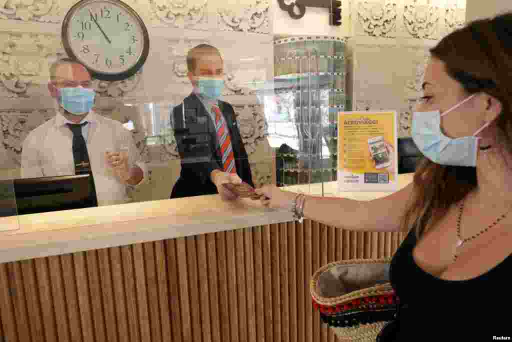 O femeie cu mască de protecție pe față arată pașaportul la stațiunea Pollina, care este primul sat de vacanță deschis în Sicilia după relaxarea măsurilor de protecție din Italia. 2 iunie 2020. REUTERS / Antonio Parrinello