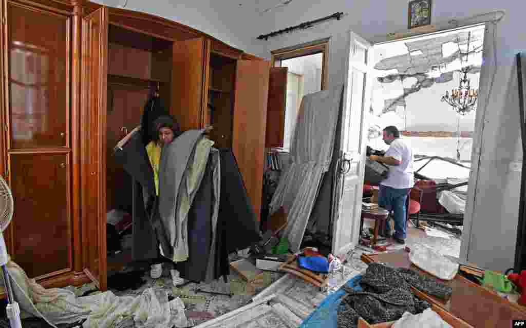 Një grua dhe një burrë po pastrojnë shtëpinë e dëmtuar.&nbsp;