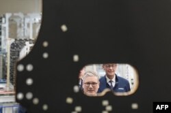 Prim-ministrul britanic Keir Starmer și cancelarul german Friedrich Merz privesc un satelit geostaționar de telecomunicații în timp ce vizitează fabrica Airbus din Stevenage, sudul Angliei, după semnarea unui tratat de cooperare bilaterală. - 17 iulie 2025