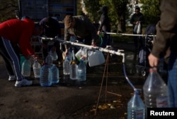 Місцеві жителі наповнюють пляшки свіжою питною водою, оскільки головний трубопровід постачання питної води до міста був пошкоджений у Херсонській області, жовтень 2022 року