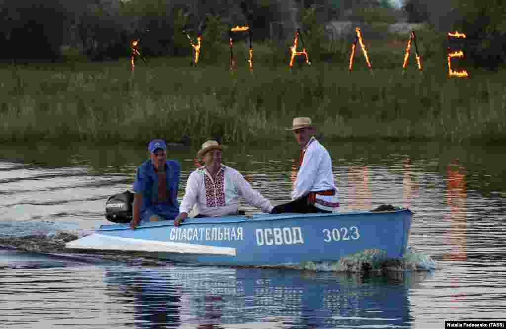 Люди в човні під час свята. Позаду них на березі &ndash; напис із палаючих букв &laquo;Купалле&raquo;