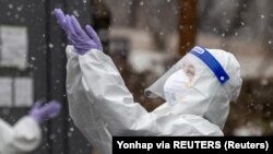 Түштүк Кореянын Сеул шаарындагы СOVID-19 полигонунда коргоочу кийимчен медкызматкер. Кар жаап жатканына кубанып турат. 