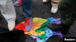 ЛГБТ қауымдастығы құқығын қорғаушылардың түрлі-түсті жалауын таптап жатқан гейлерге қарсы белсенділер. (Көрнекі сурет.)