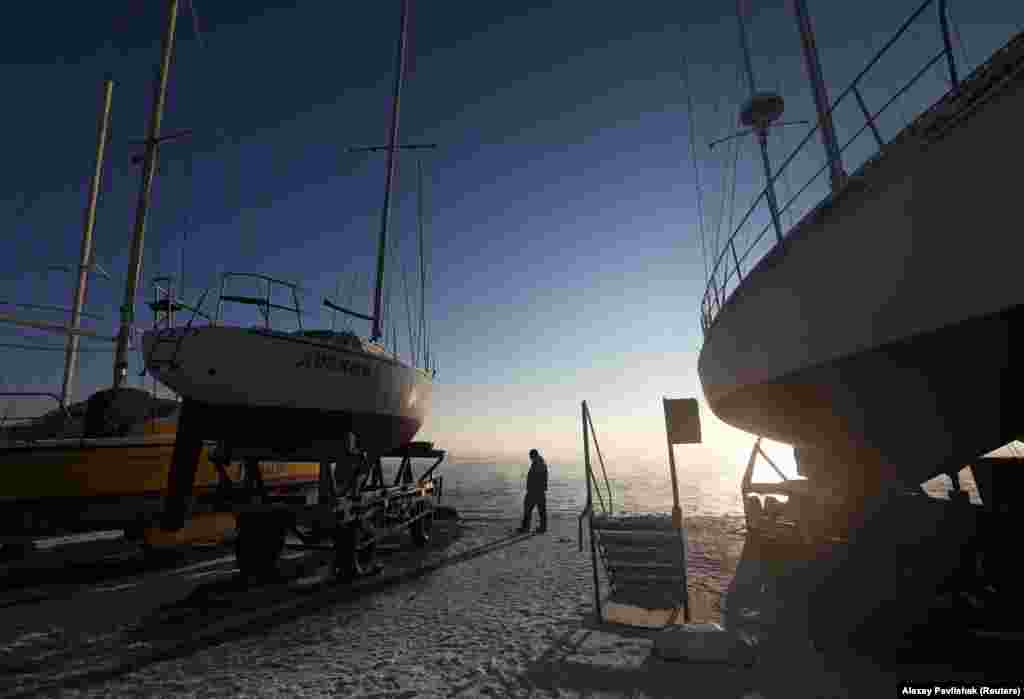 Мужчина проходит мимо лодок на берегу Черного моря в Евпатории