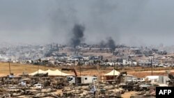 Це фото, зроблене з позиції на півдні Ізраїлю на кордоні з сектором Гази, показує ізраїльські танки та бульдозери, розгорнуті на тлі клубів диму над зруйнованими будівлями в Газі під час ізраїльського бомбардування, 17 травня 2025 року.