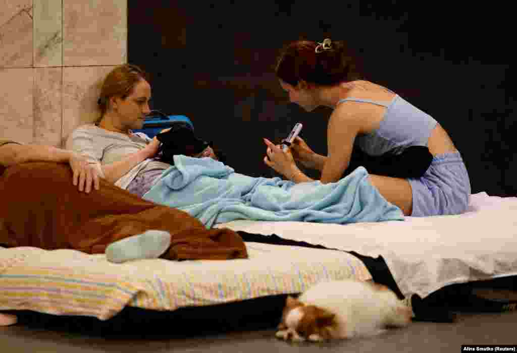 Dy gra duke shikuar ekranin e një telefoni mobil, teksa një qen pushonte pranë tyre, brenda një stacioni metroje, gjatë një alarmi për sulme, më 8 korrik.