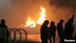 Силуэты людей на фоне горящей патрульной машины