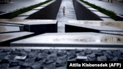 Maszkos látogató nézi a Parlament szomszédjában lévő Trianon-emlékművet 2021. január 19-én. 