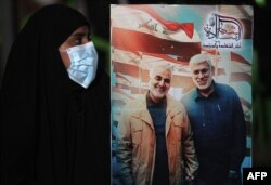 Iraki nő transzparensével, 2020. január 2-án. Ezen Abu Mahdi al-Muhandis iraki milíciavezér is szerepel, aki Szolejmáni tábornokkal együtt vesztette életét 2019 elején.