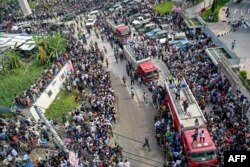 Oamenii se înghesuie pe o stradă, în timp ce autospecialele de stingere a incendiilor rămân în așteptare în fața școlii unde un avion de antrenament al Forțelor Aeriene s-a prăbușit în Dhaka, pe 21 iulie 2025.