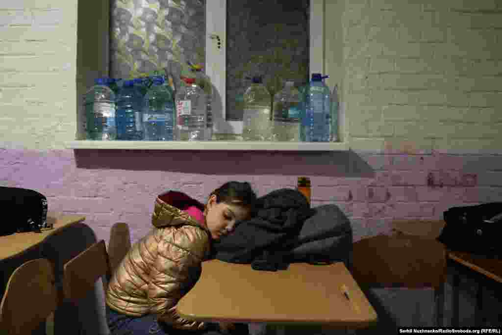 Një vajzë fle në një strehim të nëndheshëm pas sulmeve ajrore.