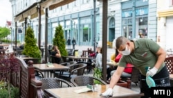 Felszolgáló fertőtlenítővel tisztítja egy étterem teraszán az egyik asztalt Nyíregyházán a Dózsa György utcában, 2020. május 4-én