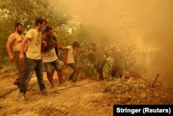 Egy tömlőt tartó férfit segítenek fel társai a tűzvésztől pusztított Guvesz faluban, Évia szigetén 2021. augusztus 8-án