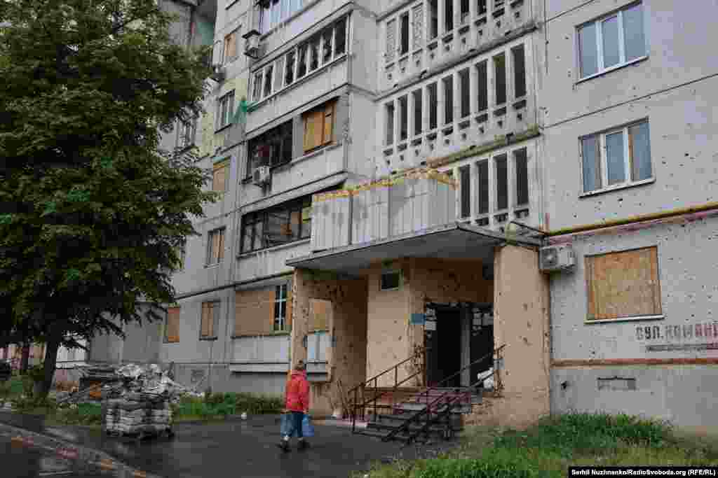 Жінка несе бутлі з водою до свого пошкодженого російськими обстрілами будинку. Зараз дім відновлюють