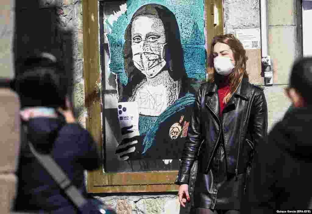 Туристка в Барселоні позує для фото поруч із графіті, на якому зображена Мона Ліза в масці під назвою &laquo;Вірус мінливого світу&raquo;. Іспанія. Весна 2020 року