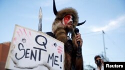 Jacob Chansley, poznat i kao Jake Angeli, drži natpis "Kju me je poslao", dok se obraća pristalicama tadašnjeg predsednika SAD Donalda Trumpa na protestu posle predsedničkih izbora, Finiks, 5. novembar 2020.