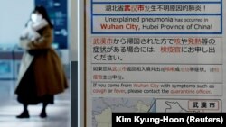 O femeie care poartă o mască trece pe lângă o notificare de carantină despre focarul de coronavirus din Wuhan, China