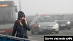 A woman walks through the smog-covered streets of Belgrade.