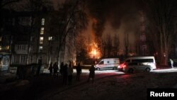 Жители се събират край жилищна сграда, докато електроцентрала гори след атака на руски безпилотен самолет в Киев на 19 декември