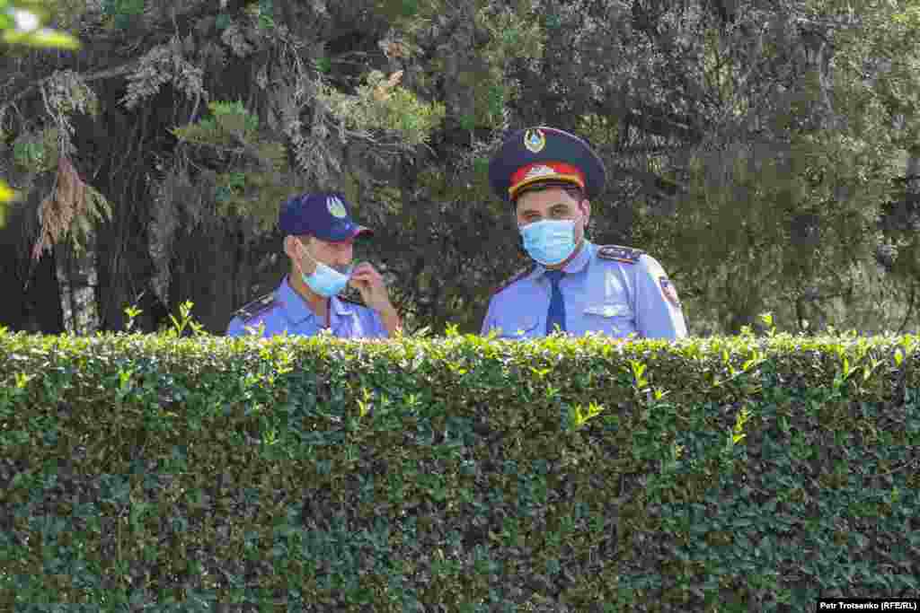 Полицейские выглядывают из-за кустов во время дежурства у акимата Алматы, 17 июля 2021 года