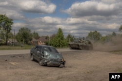 Українська самохідна гаубиця 2С1 «Гвоздика» проїжджає повз пошкоджене авто на дорозі у Вовчанському районі Харківської області, 12 травня 2024 року