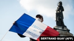 Un bărbat cu steagul francez în timpul unei demonstrații în Place de la Republique din Paris, 18 octombrie 2020, în amintirea profesorului Samuel Paty care a fost decapitat