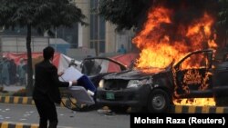 A lawyer throws a trash can toward police near a vehicle set on fire outside the Punjab Institute of Cardiology (PIC) in Lahore on December 11.